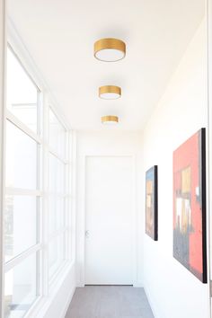 an empty hallway with two paintings on the wall and one light fixture hanging from the ceiling