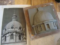 two pictures of buildings are shown on the table next to each other, one is made out of clay