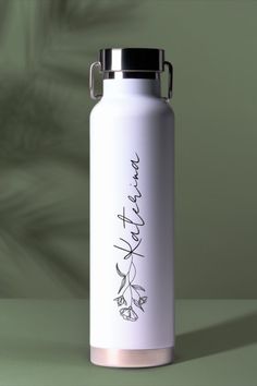 a stainless steel water bottle with writing on the front and side, sitting on a green surface