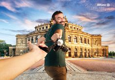 a man pointing his camera at someone in front of a building with a sky background