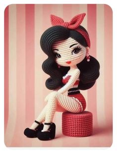 a crocheted doll sitting on top of a red stool next to a pink striped wall