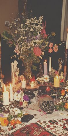 a table topped with lots of candles next to a vase filled with flowers and plants