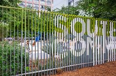 a metal fence with the word zoo painted on it in front of some trees and bushes