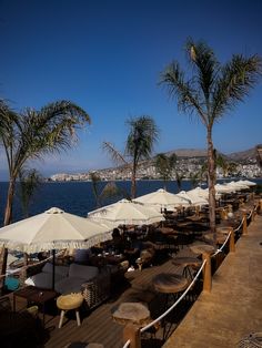 tables and umbrellas are lined up on the deck by the ocean with palm trees