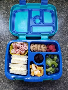 a blue lunch box filled with fruit, crackers and other food on top of a table