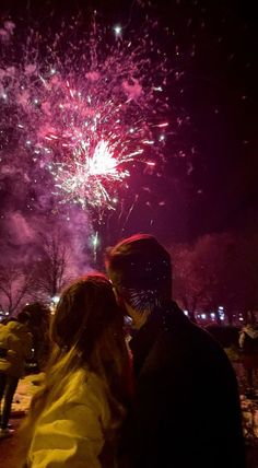 two people standing next to each other with fireworks in the background