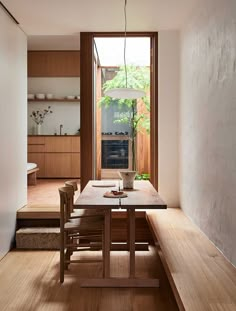 a wooden table sitting under a window next to a kitchen area with stairs leading up to it