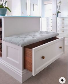 a white bench with drawers underneath it and a potted plant in the corner next to it