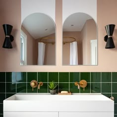 two mirrors above a white sink in a room with green tiled walls and flooring