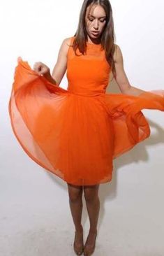 a woman in an orange dress is holding her hands out to the side and looking down