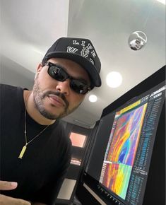 a man wearing sunglasses and a hat in front of a computer screen with an image on it