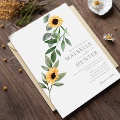 a wedding card with sunflowers and greenery on the front, sitting on a wooden table