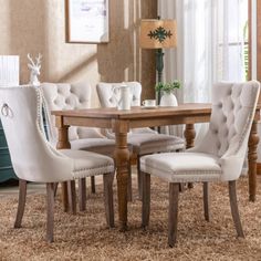 a dining room table with white chairs and a rug on the floor in front of it