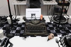 a table topped with black and white plates covered in typewriters next to cupcakes