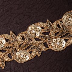 a close up of a gold colored lace with flowers and leaves on the side,