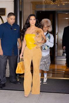 a woman in yellow is holding a small dog while walking out of a building with other people