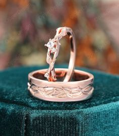 two wedding rings sitting on top of a green velvet covered cushioned surface, one with an intricate design in the middle