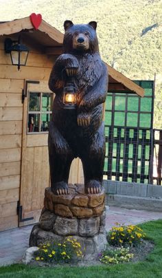 a statue of a bear holding a lantern in front of a wooden cabin with mountains in the background