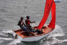 two men on a small sailboat in the water with one man pointing at something