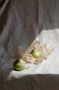 two green apples sitting on top of a white cloth