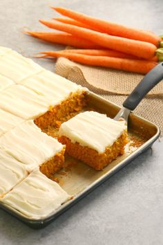 carrot cake with white frosting in a pan and carrots next to the tray