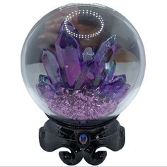 a purple crystal ball on top of a black stand with lights in the middle and crystals inside