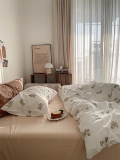 an unmade bed with white sheets and pillows in front of a curtained window