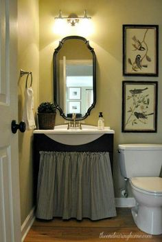 a white toilet sitting next to a sink in a bathroom under a mirror and framed pictures on the wall