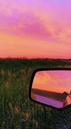 a rear view mirror on the side of a car with a sunset in the background