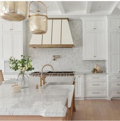 a kitchen with marble counter tops and white cabinets, gold accents on the hoods