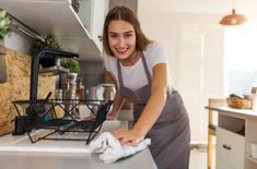 a woman in an apron is cleaning the counter top with a rag and smiling at the camera