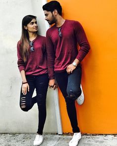 a man and woman standing next to each other in front of an orange wall wearing red sweaters