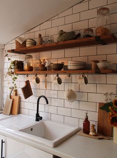 a kitchen with white tiled walls and shelves filled with dishes on the shelf above the sink