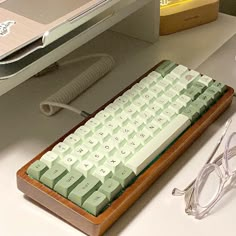 a computer keyboard sitting on top of a desk next to a pair of eyeglasses