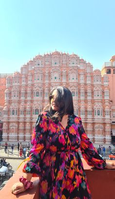 a woman in a colorful dress is standing on a balcony looking at the building behind her