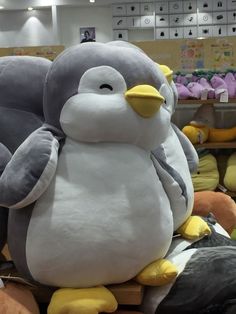 a large stuffed penguin sitting on top of a pile of stuffed animals in a store