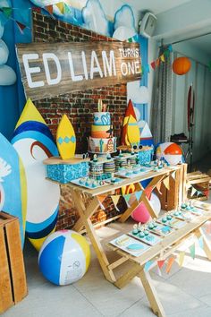 an outdoor birthday party with balloons, cake and cupcakes on a table in front of a brick wall