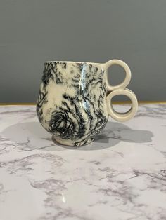 a white and black coffee cup sitting on top of a marble counter next to a pair of scissors