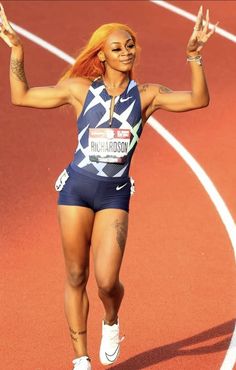 a woman running on a track with her arms in the air and one hand up