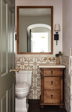 a white toilet sitting next to a wooden cabinet in a bathroom under a large mirror