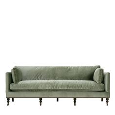 a green velvet couch with wooden legs and pillows on the back, in front of a white background