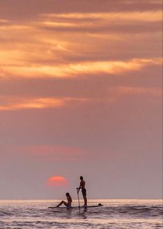 two people are paddle boarding in the ocean at sunset or dawn with one person on a surfboard