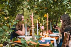 two women sitting at a table with plates and wine glasses in front of them, surrounded by greenery