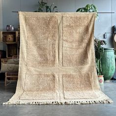 a large tan blanket sitting on top of a floor next to a potted plant