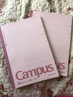 two pink notebooks sitting next to each other on top of a floral covered bed