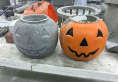 three pumpkin shaped vases sitting on top of a cement table next to each other