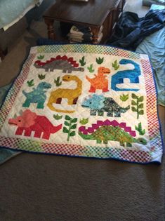 a child's quilt on the floor with an elephant, dinosaur and giraffe design