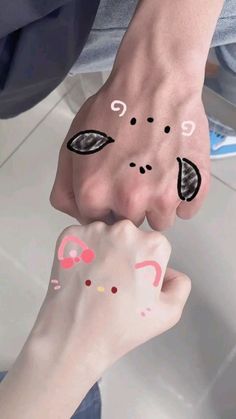 two hands with faces painted on them and one holding the other hand up to their face