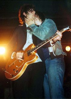 two people kissing while playing guitar on stage