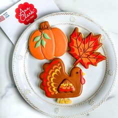 three decorated cookies on a plate with fall leaves and pumpkins in the background, along with an envelope